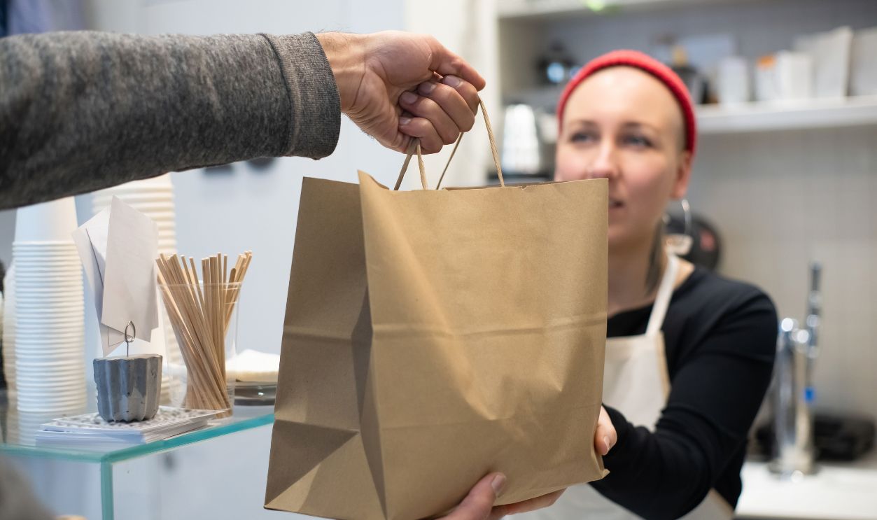Woman handing a takeaway bag to a customer in a Portuguese café.