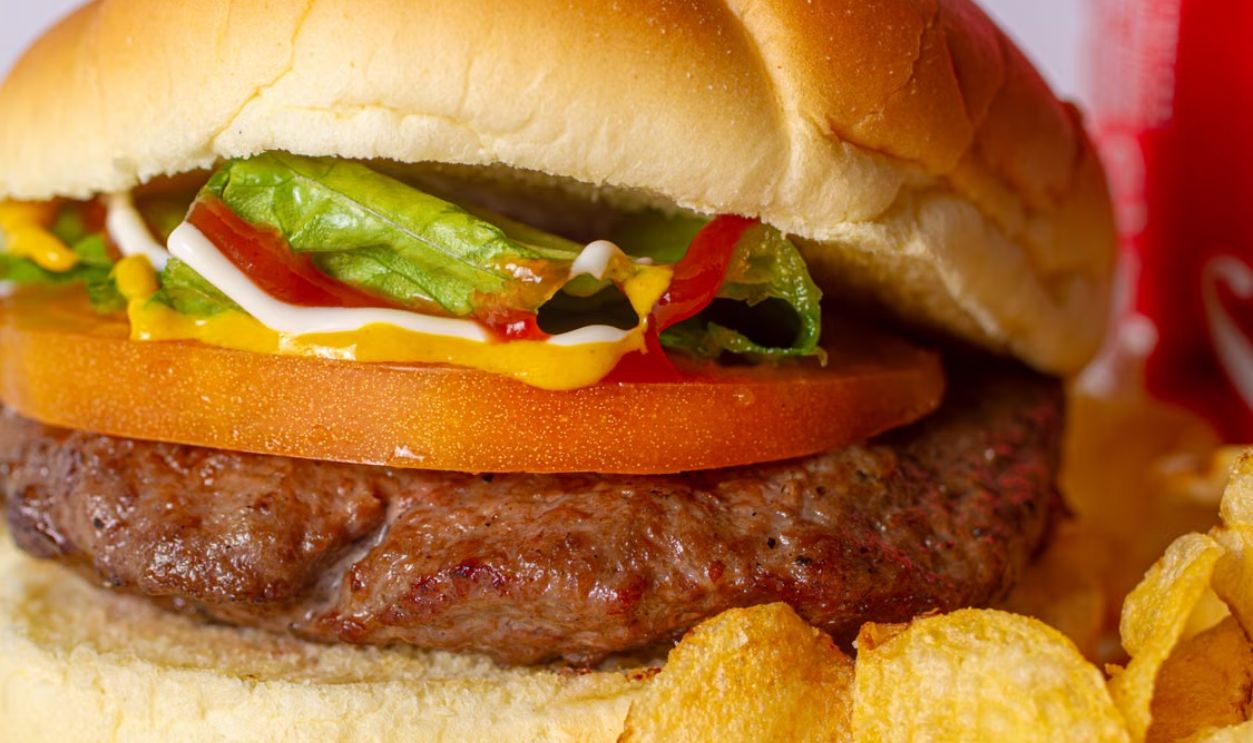 Close-up of a juicy cheeseburger with lettuce, tomato, and sauces, served with potato chips