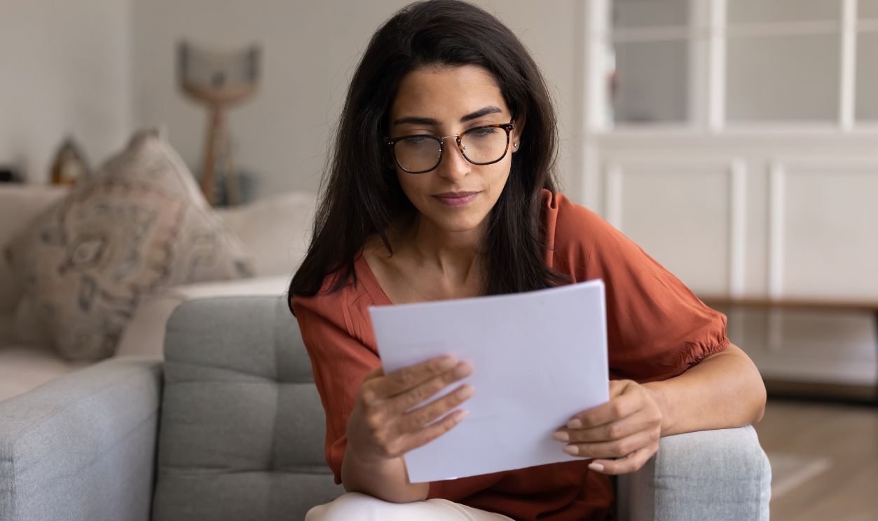 Shutterstock-2694519725, Focused smart Hispanic homeowner woman in glasses checking bills for payment at home, reading paper financial report, invoice, legal document, getting formal confirmation letter