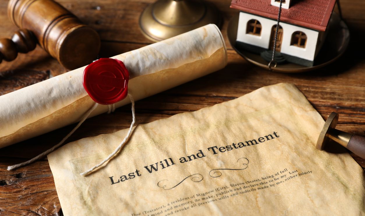 Last Will and Testament, gavel, scroll and house model on wooden table, closeup