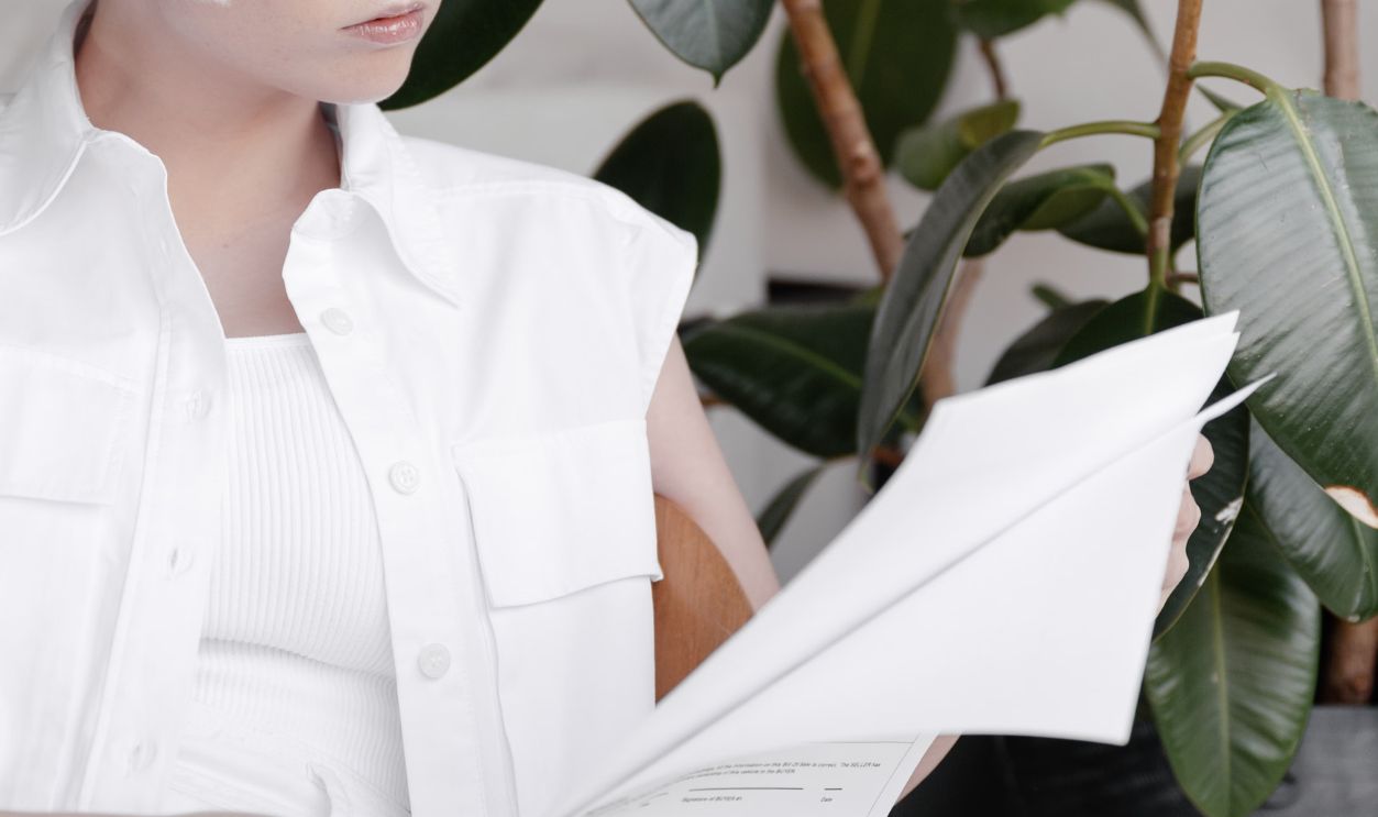 A woman with platinum hair reads a document in a stylish, plant-filled interior.