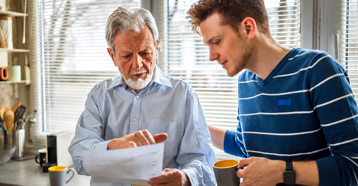 Senior father and adult son carefully going over documents in their kitchen