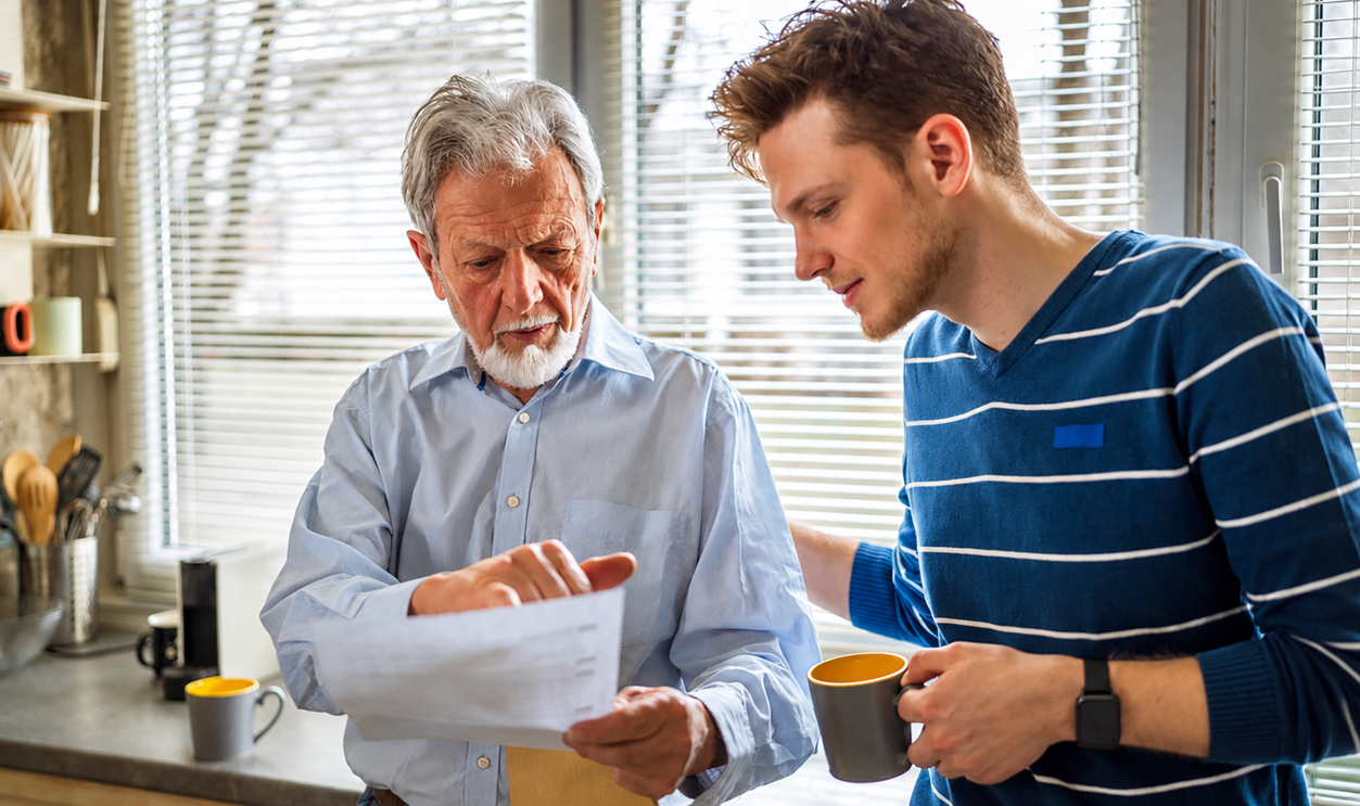 Senior father and adult son carefully going over documents in their kitchen