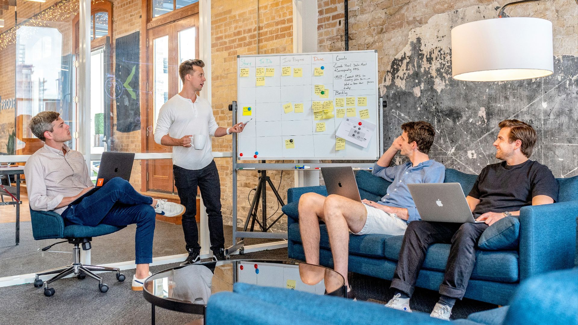 three men sitting while using laptops and watching man beside whiteboard