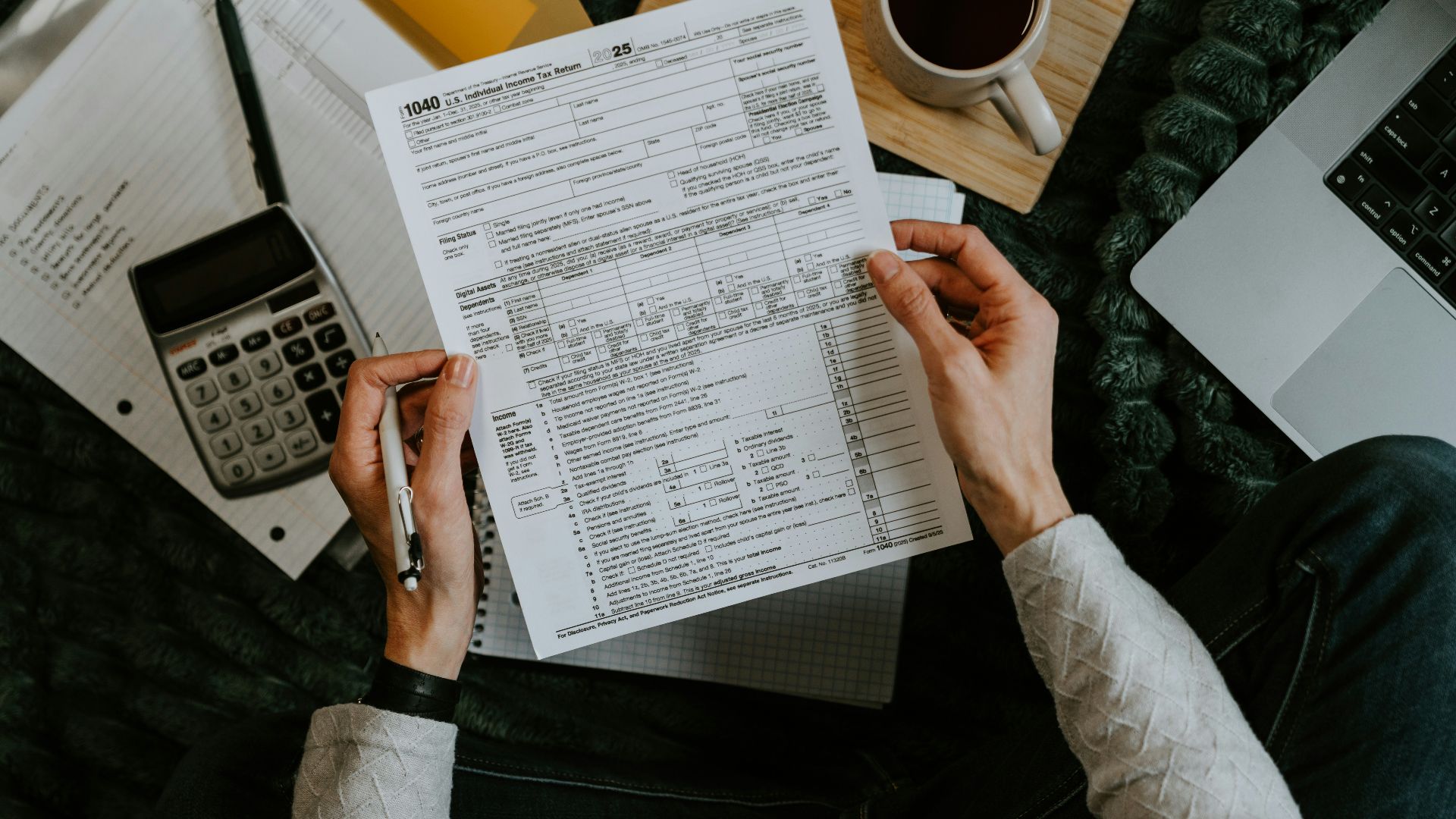 Hands holding tax forms with calculator and laptop