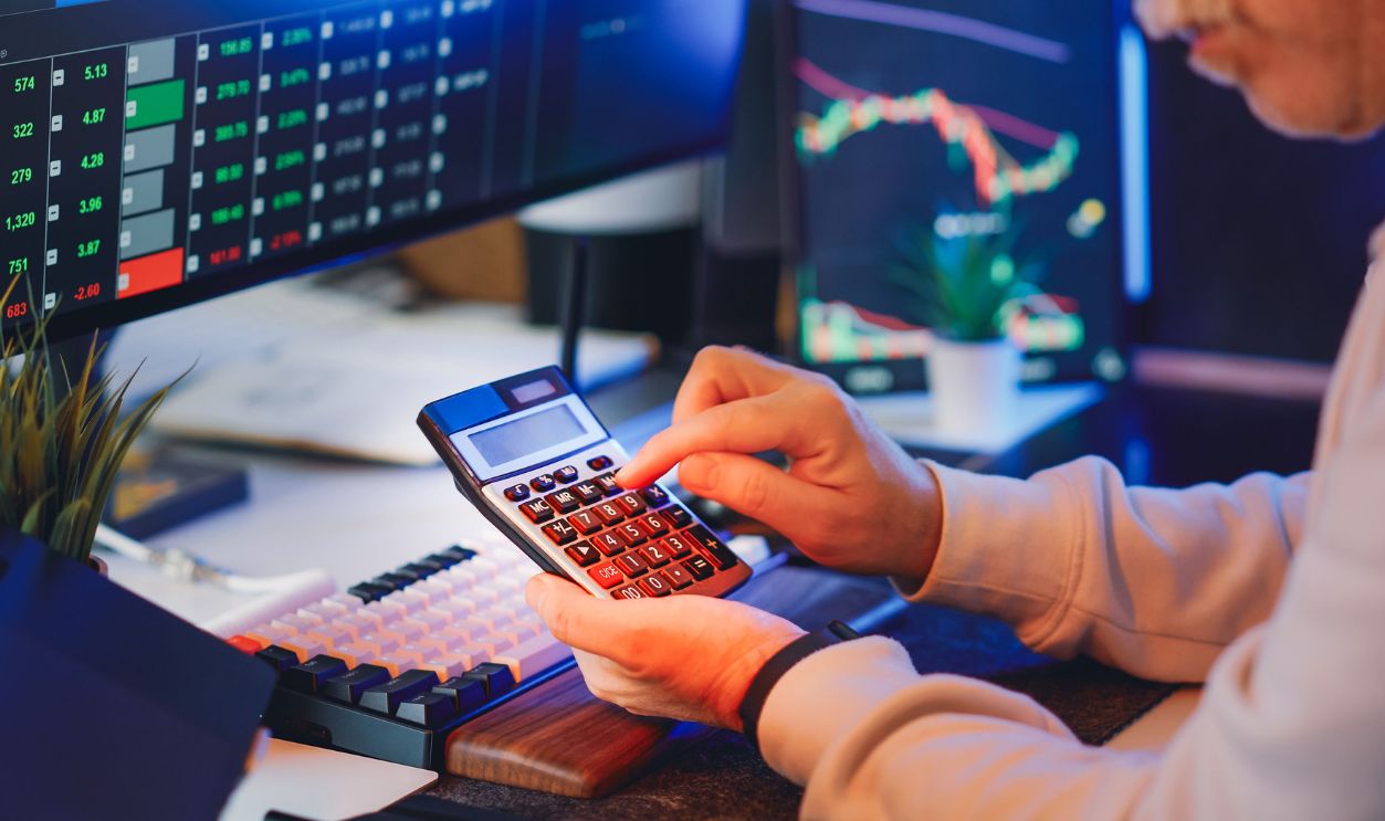 Person using a calculator in a digital office for stock market analysis.