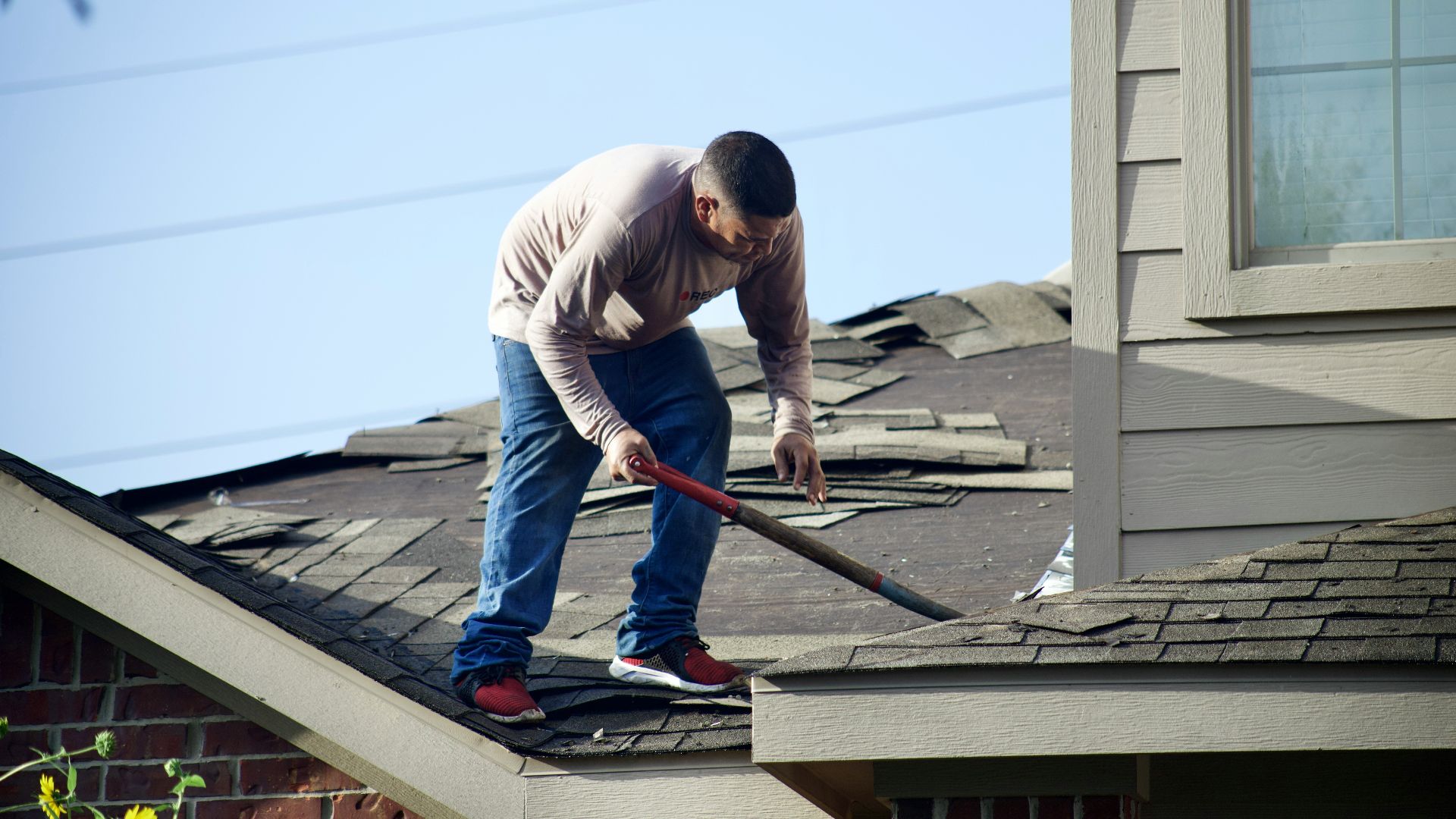 A person in a long-sleeved shirt removing shingles from a residential roof