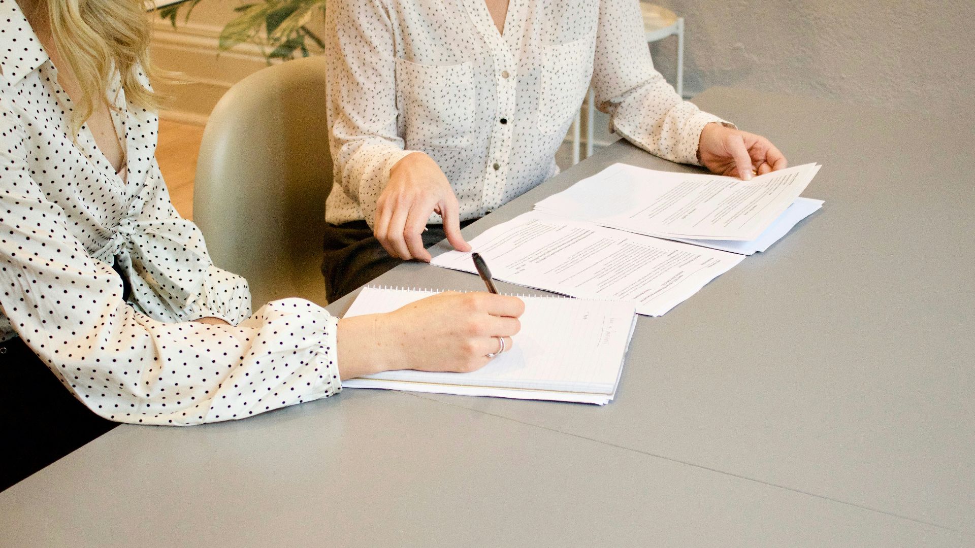 woman signing on white printer paper beside woman about to touch the documents