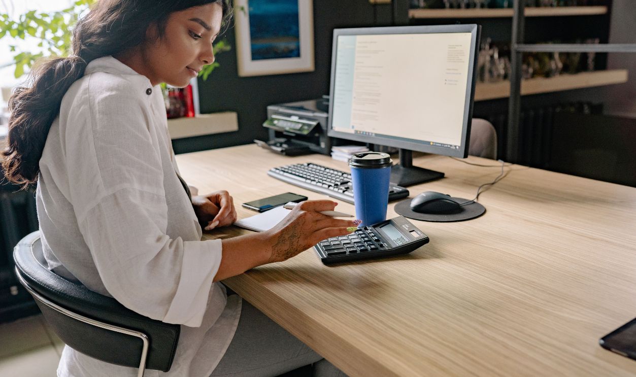 A professional woman using a calculator and computer at an office desk