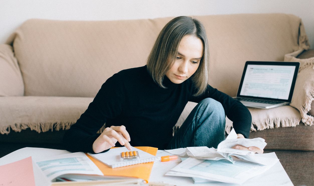 Young woman handling financial tasks with papers and laptop in cozy living room.