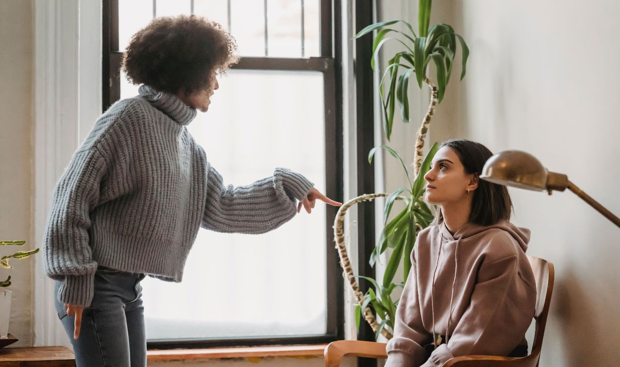 Women passionately discussing a conflict or argument in a cozy room setting.