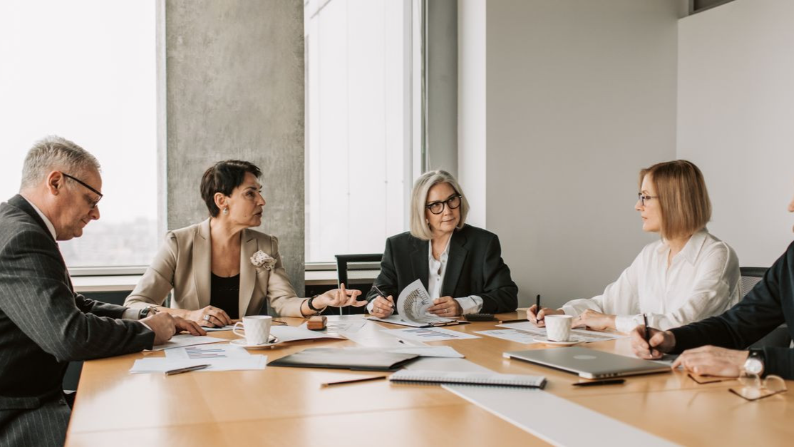 Five business professionals engaged in a meeting in a modern office setting, discussing documents and ideas.