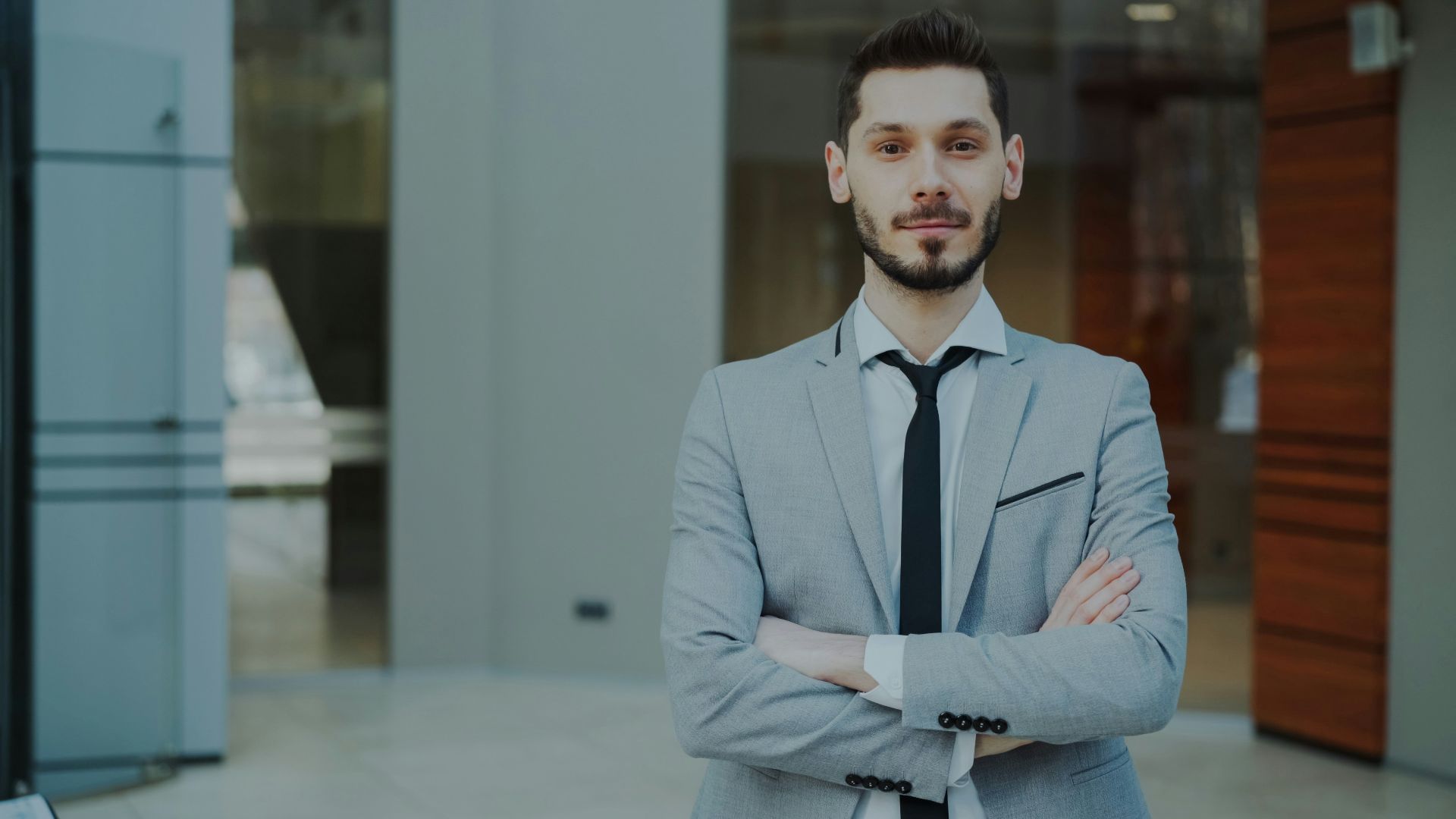A man in a suit with arms crossed stands confidently