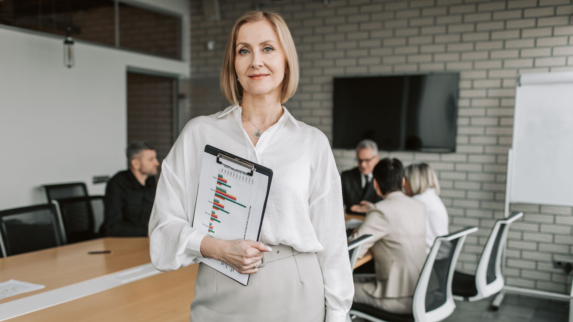 Professional businesswoman holding a clipboard during an office meeting, showcasing leadership in a corporate environment.