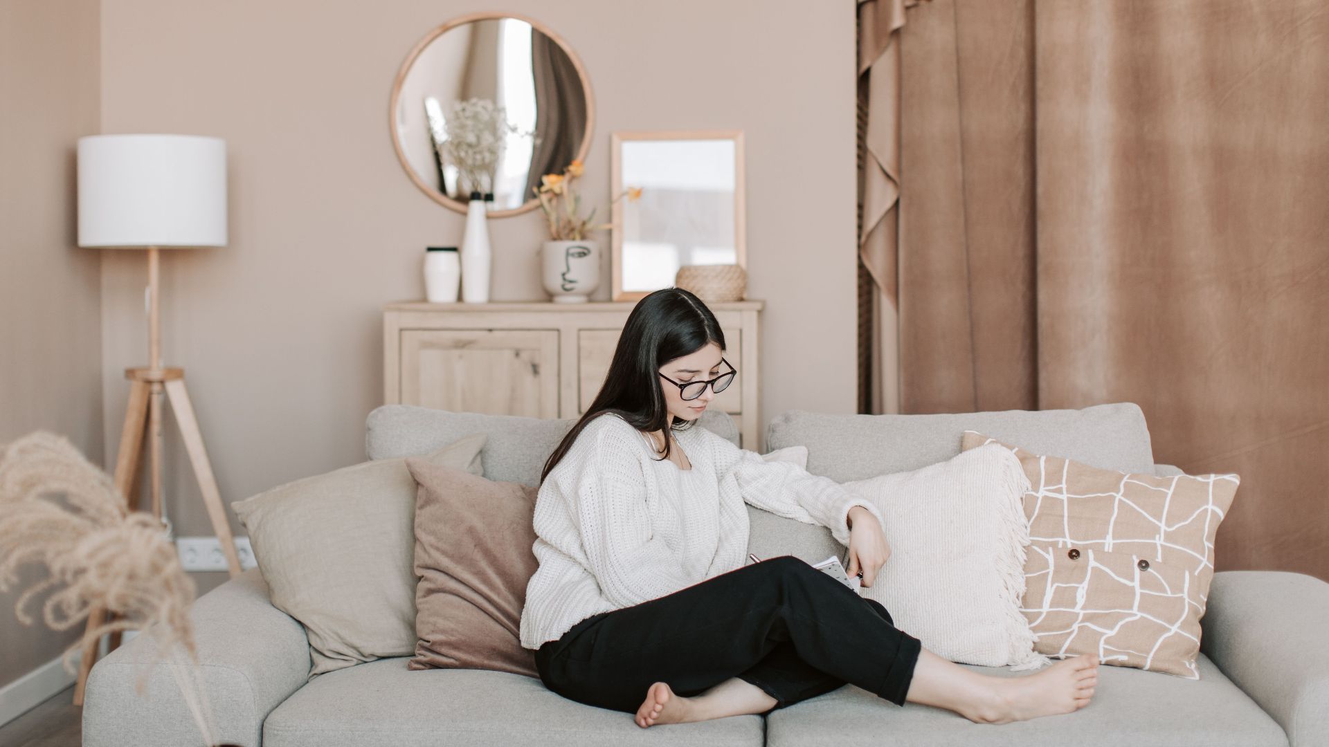 Young woman writing in notebook while sitting on a cozy sofa at home.