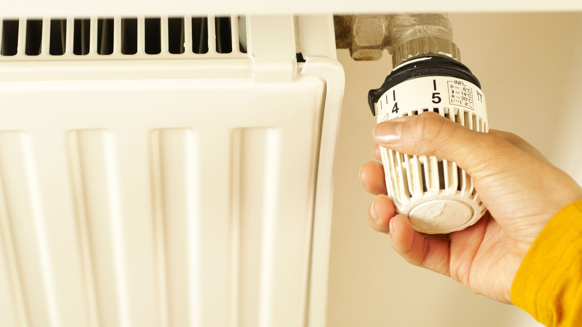 Close-up of hand adjusting radiator thermostat to control home heating temperature.