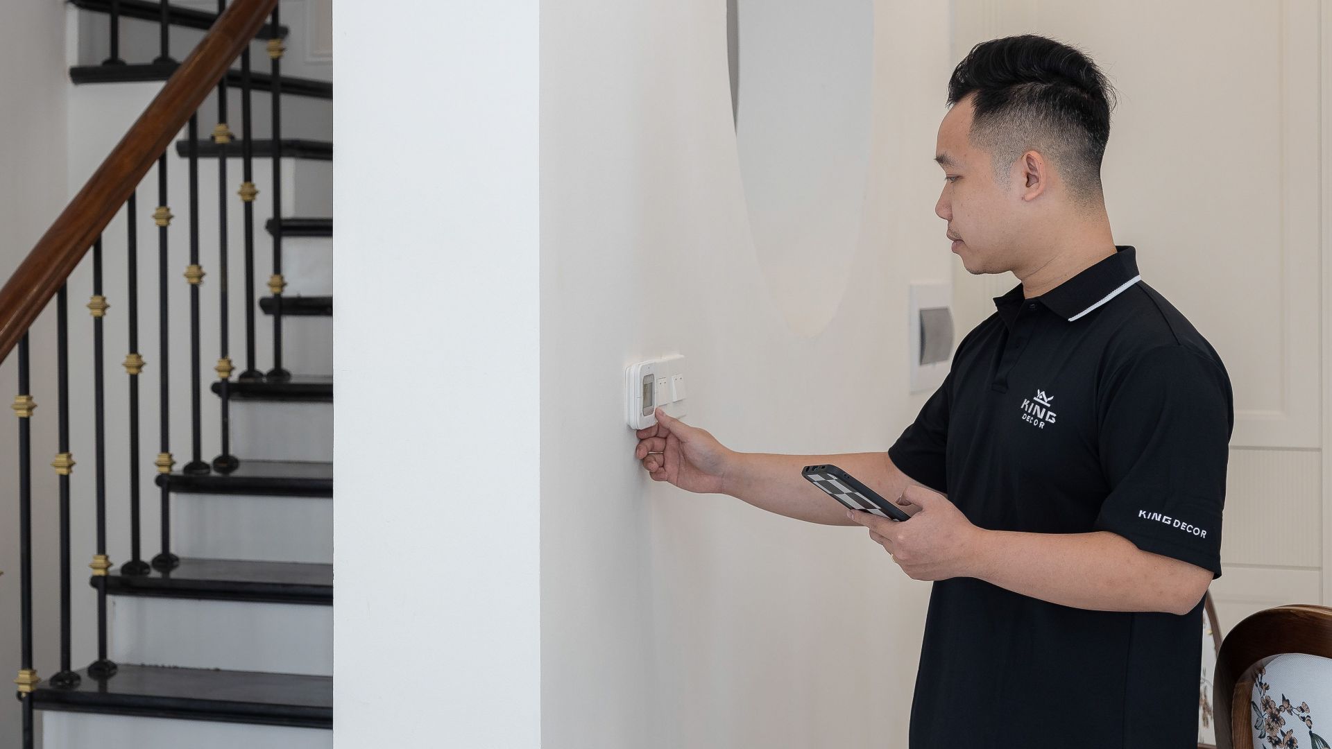 Man adjusting thermostat in stylish home with elegant staircase.