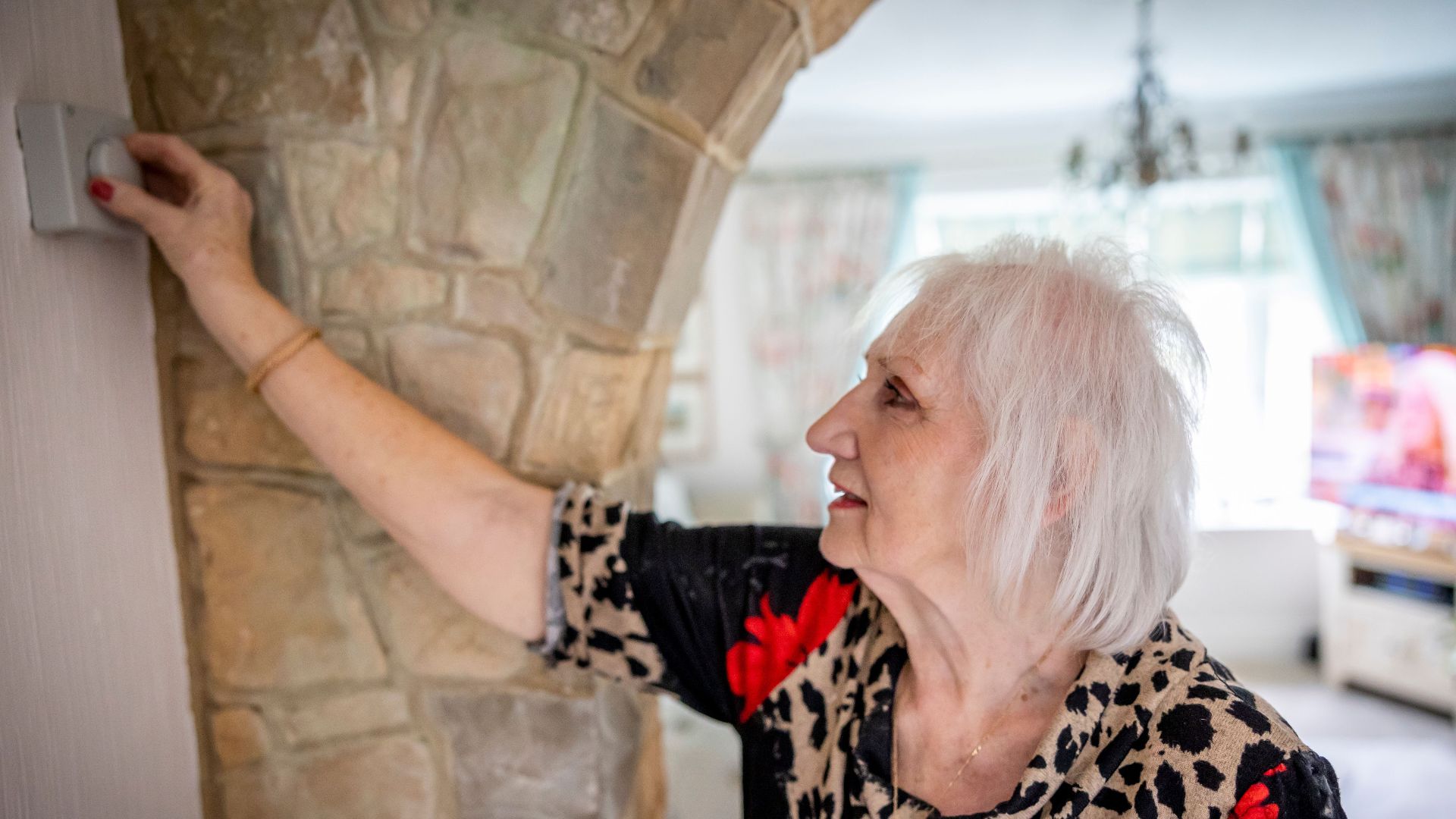 Elderly woman with gray hair adjusting temperature controller indoors.