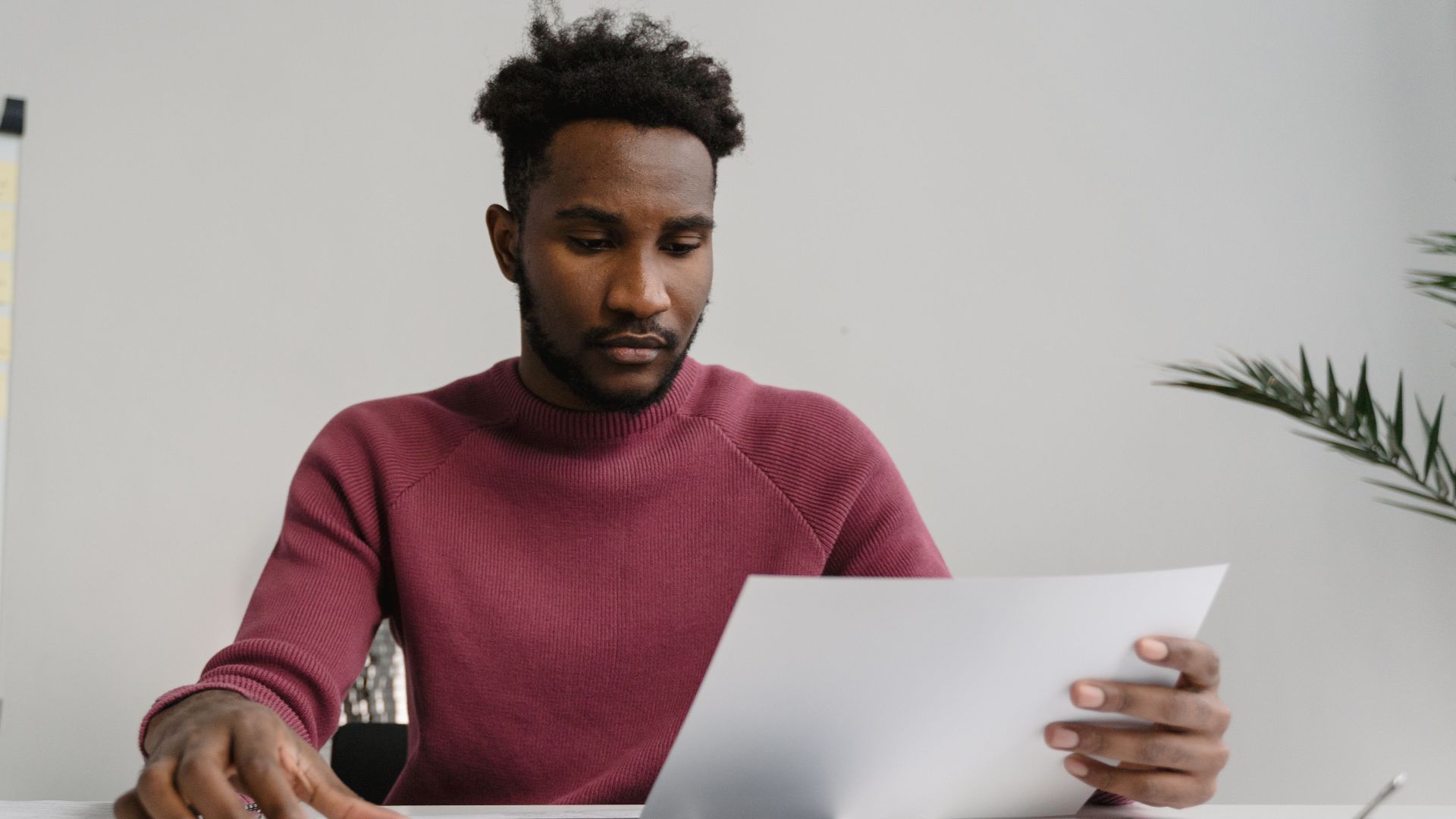 A man in a workspace analyzing a white document attentively. Modern office environment.