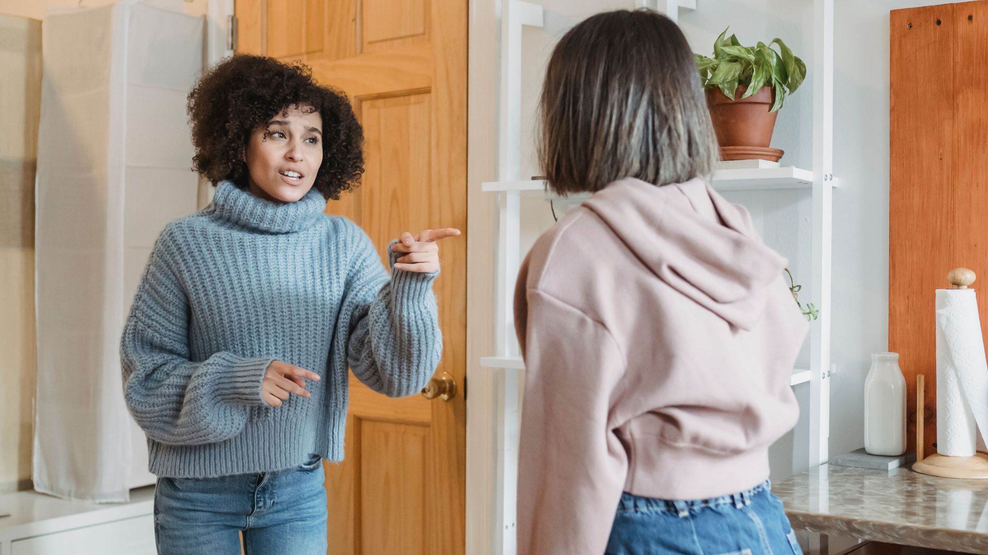 Angry African American female complaining and pointing at faceless female while having fight i modern flat with green plants