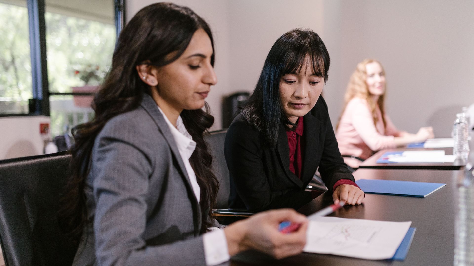 Two businesswomen discussing documents at a corporate meeting in an office setting.