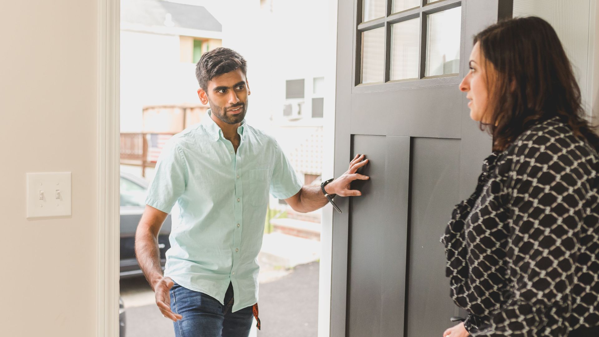 A man enters a home, conversing with a woman standing nearby in a casual setting.