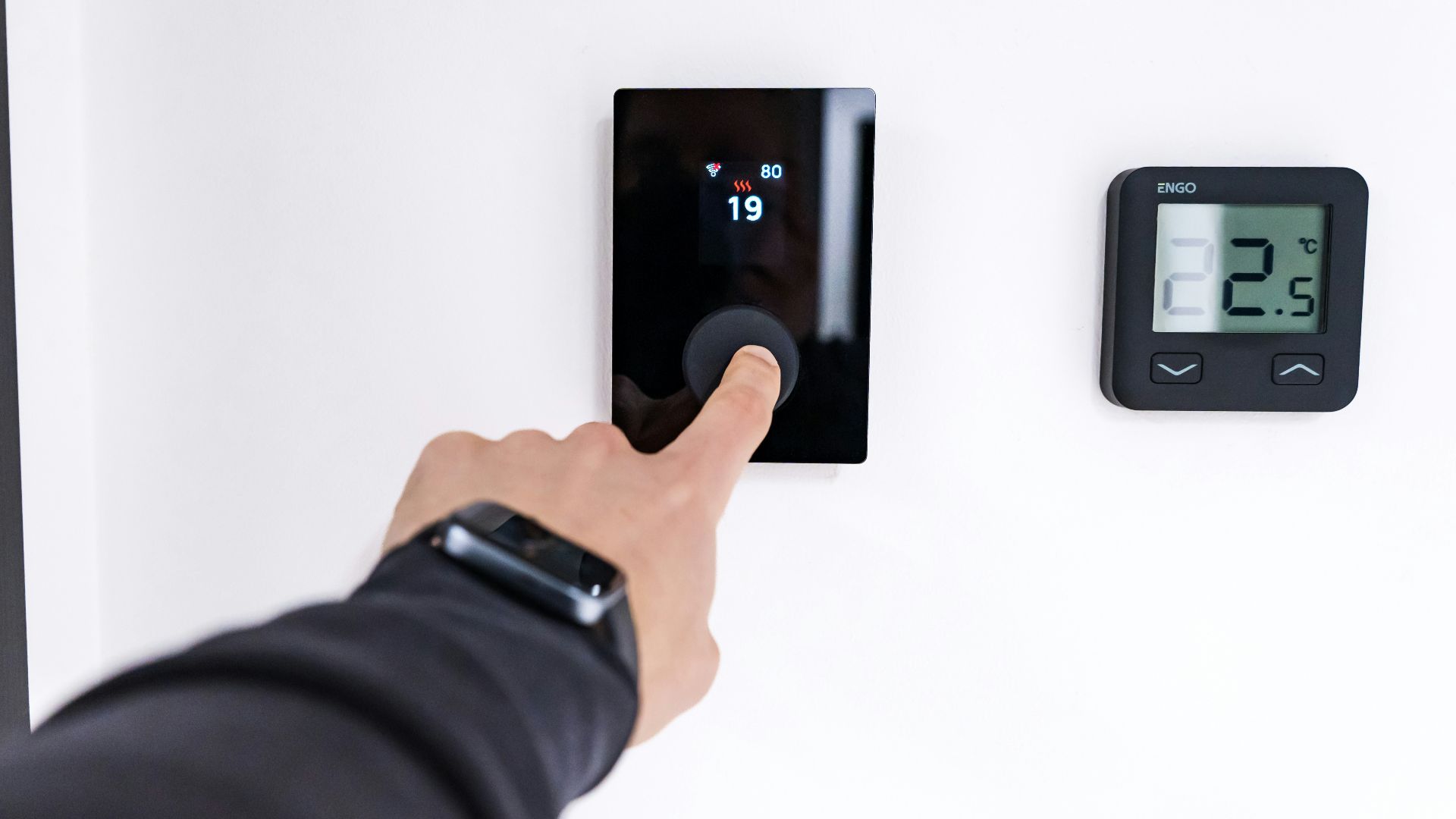 Finger adjusting a modern digital thermostat on wall