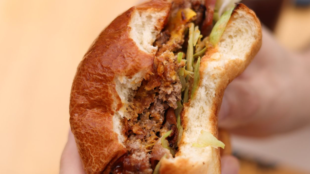 Close-up of a person holding a juicy cheeseburger with visible layers and ingredients