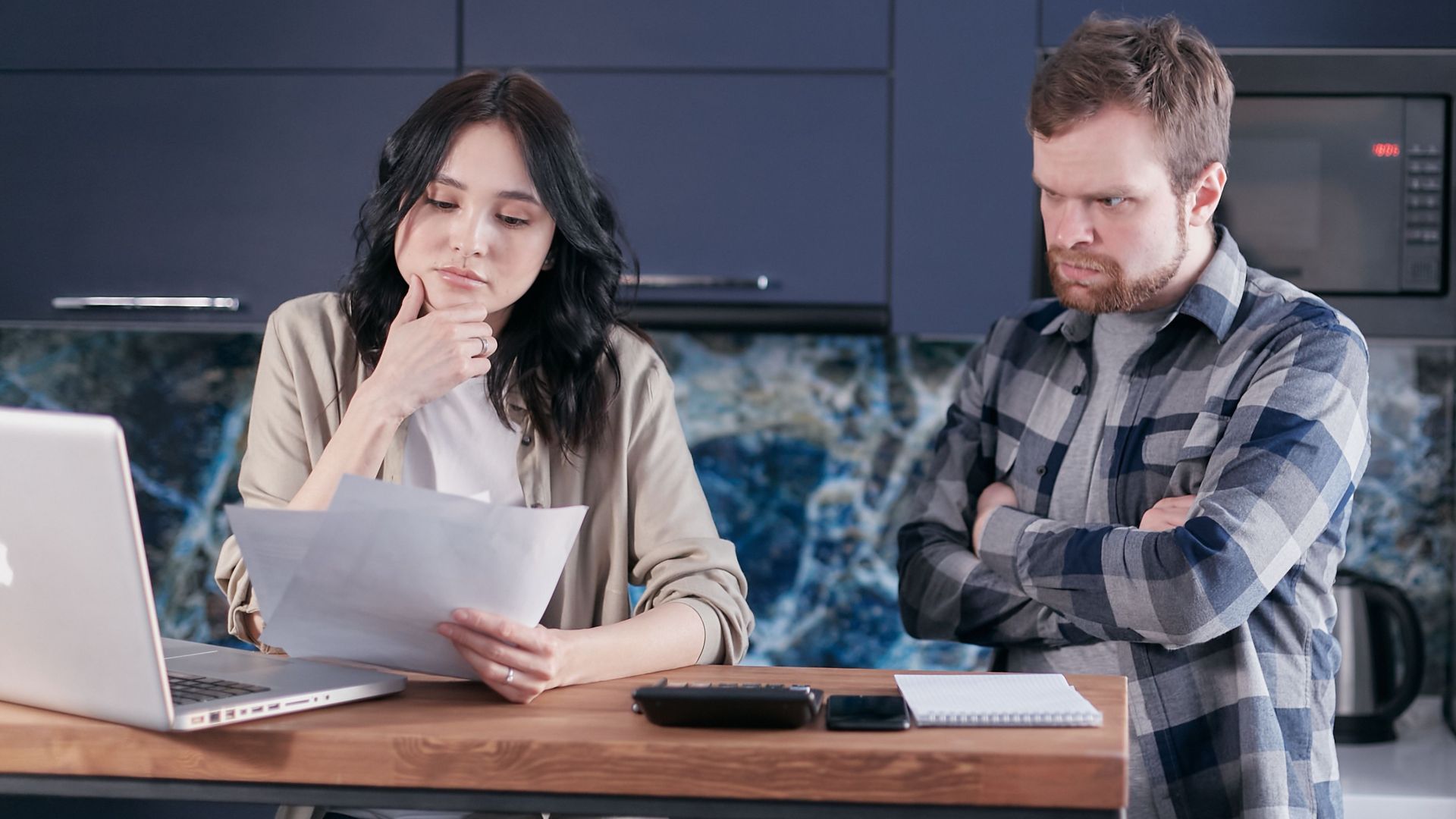 A couple sitting at a kitchen desk reviewing financial documents, using a laptop.