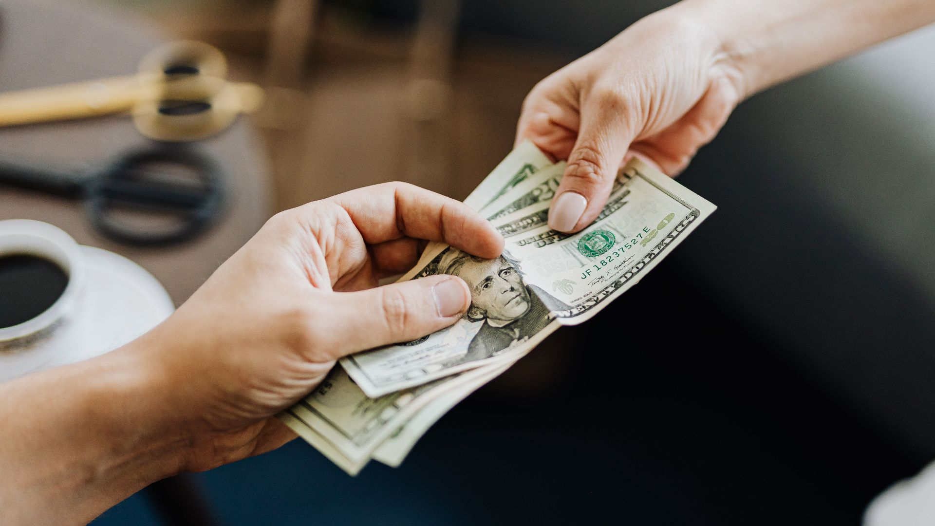 A close-up image of hands exchanging US dollar bills, symbolizing financial transaction or payment.