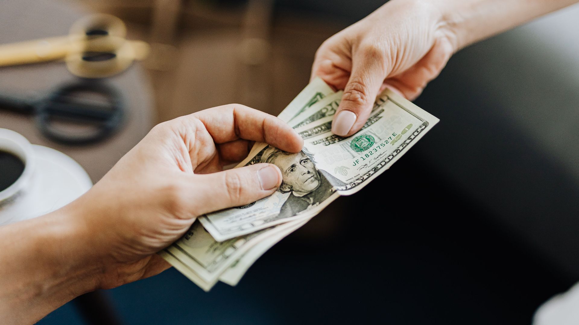 A close-up image of hands exchanging US dollar bills, symbolizing financial transaction or payment.