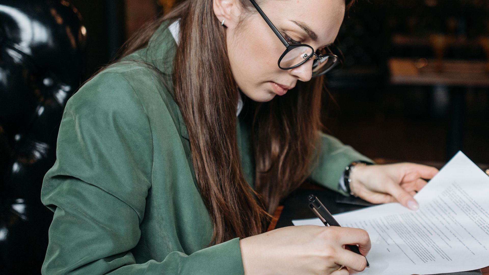 Focused businesswoman in green attire signing important documents at her desk.
