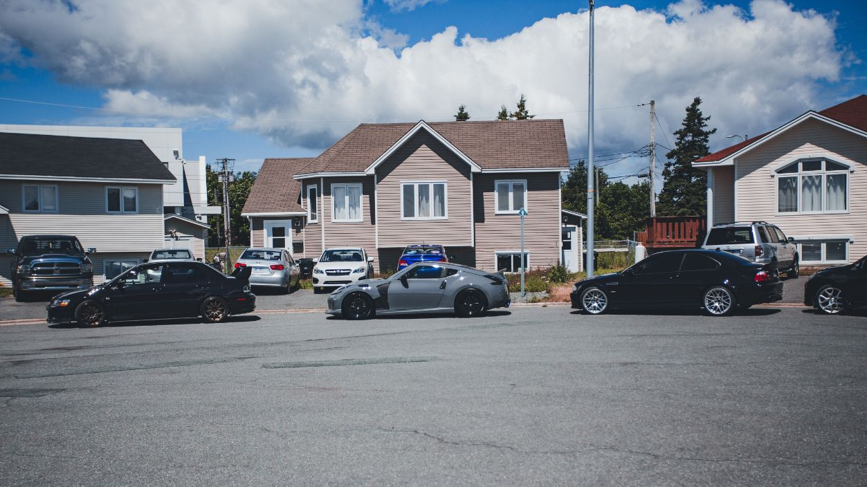 Sunny neighborhood street with modern homes and parked vehicles on a bright day.