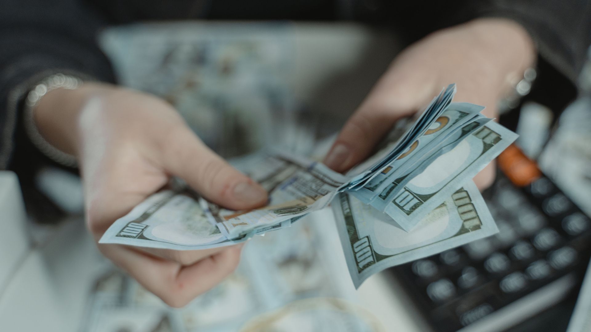 Close-up of hands counting hundred dollar bills with a calculator in the background.