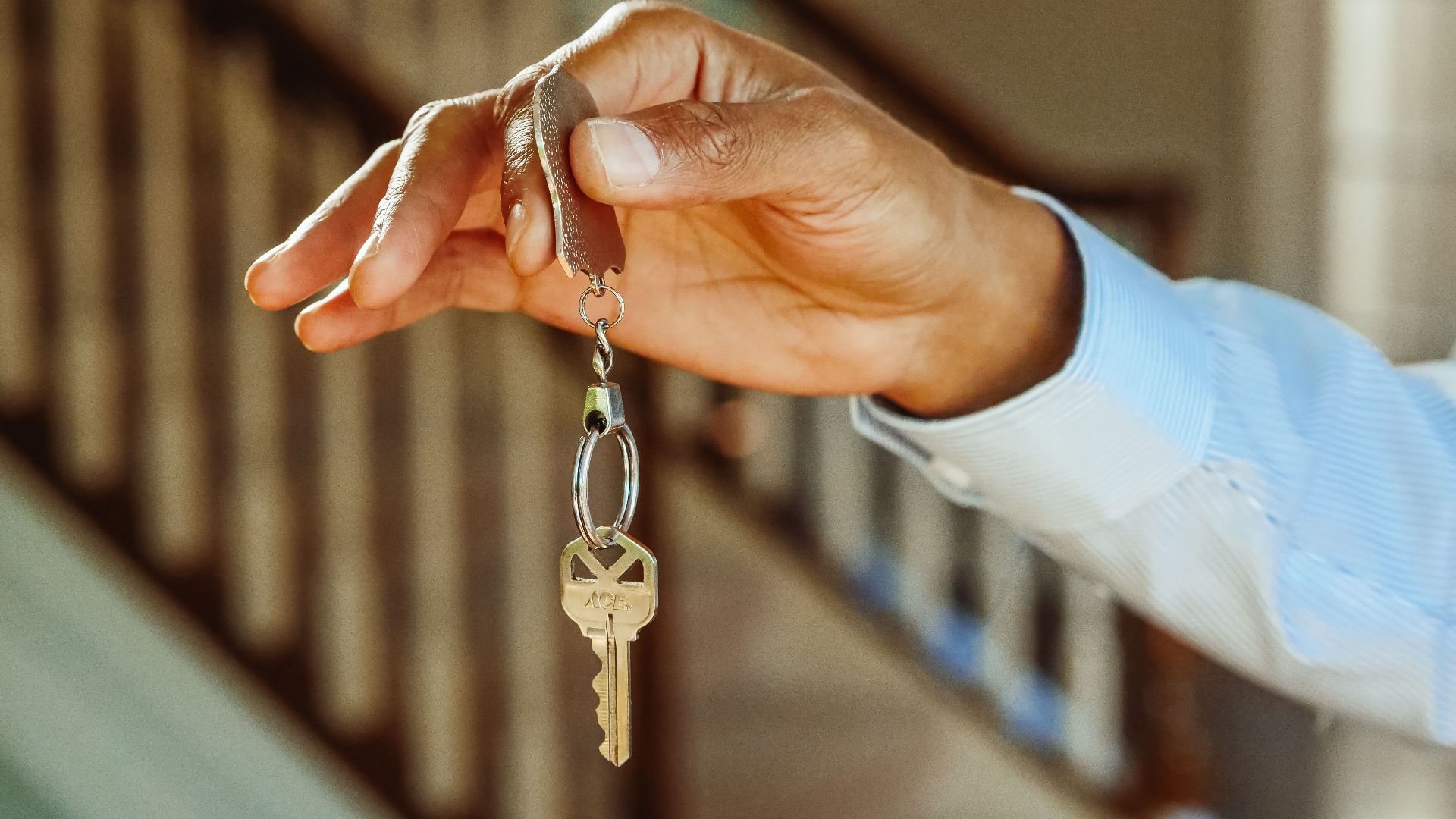 A close-up shot of a hand holding a house key, indicating new ownership or rental.
