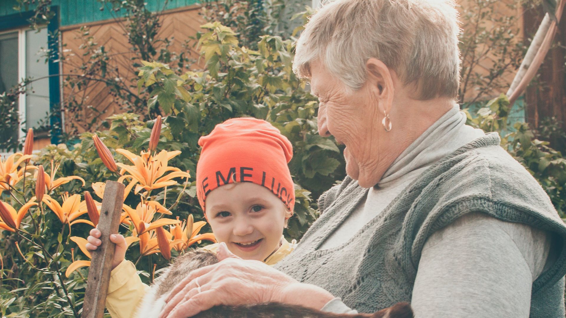 Grandmother and child enjoying time with a cat in a sunlit garden.