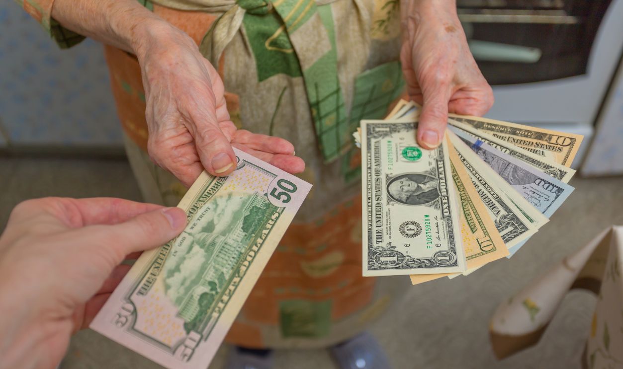 Dollars in the hand of an elderly woman pensioner in the kitchen in the apartment