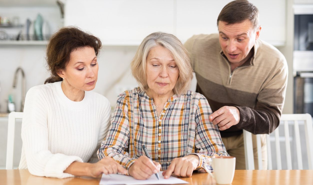 Shutterstock-2402830983, Old woman deciding and signing inheritance papers in family circle