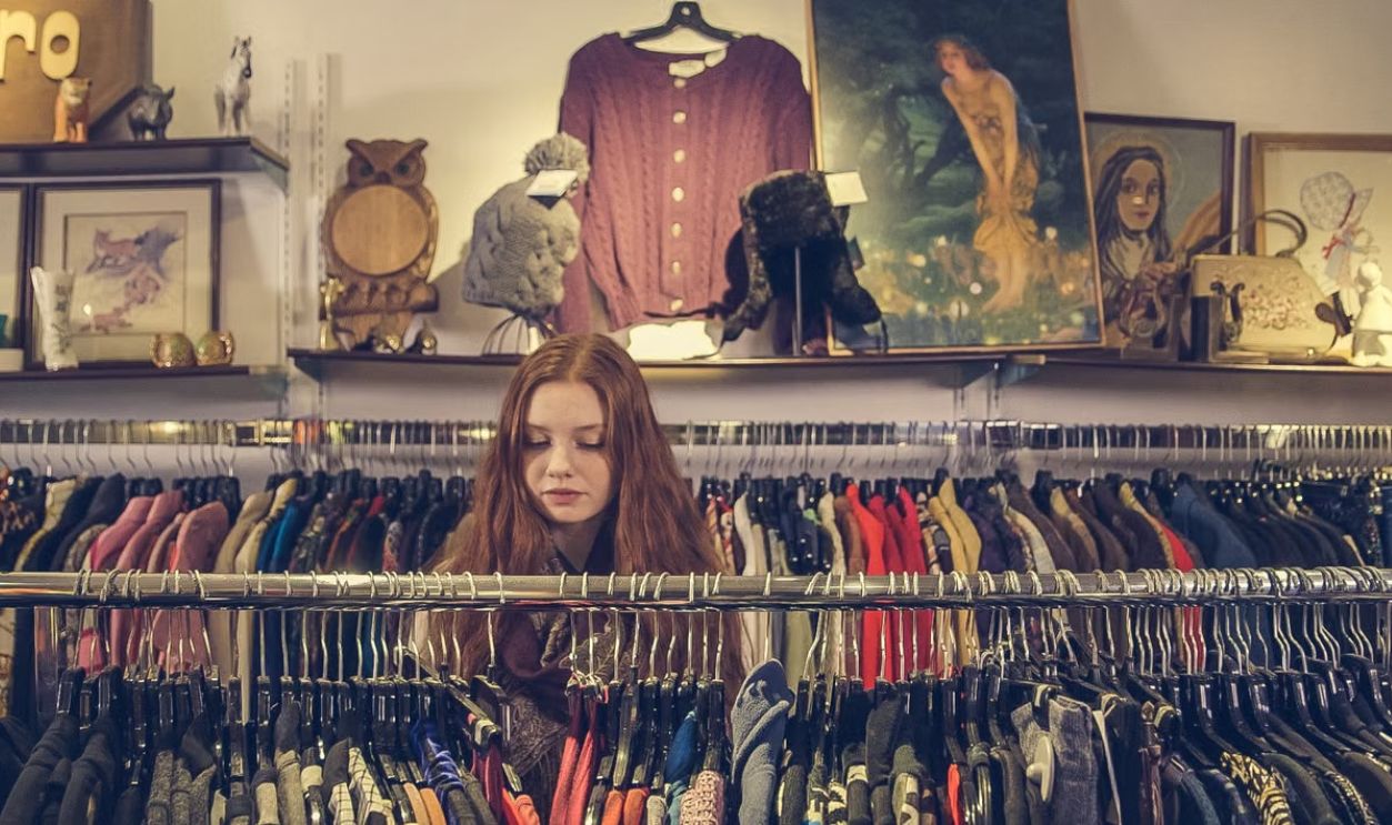 A woman explores racks of clothing in a cozy vintage shop with eclectic decor.
