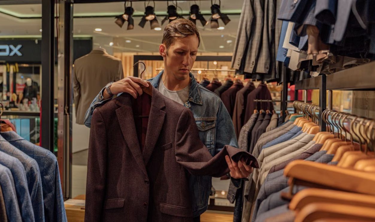 Man browsing stylish blazers in a modern clothing store, considering fashion options.