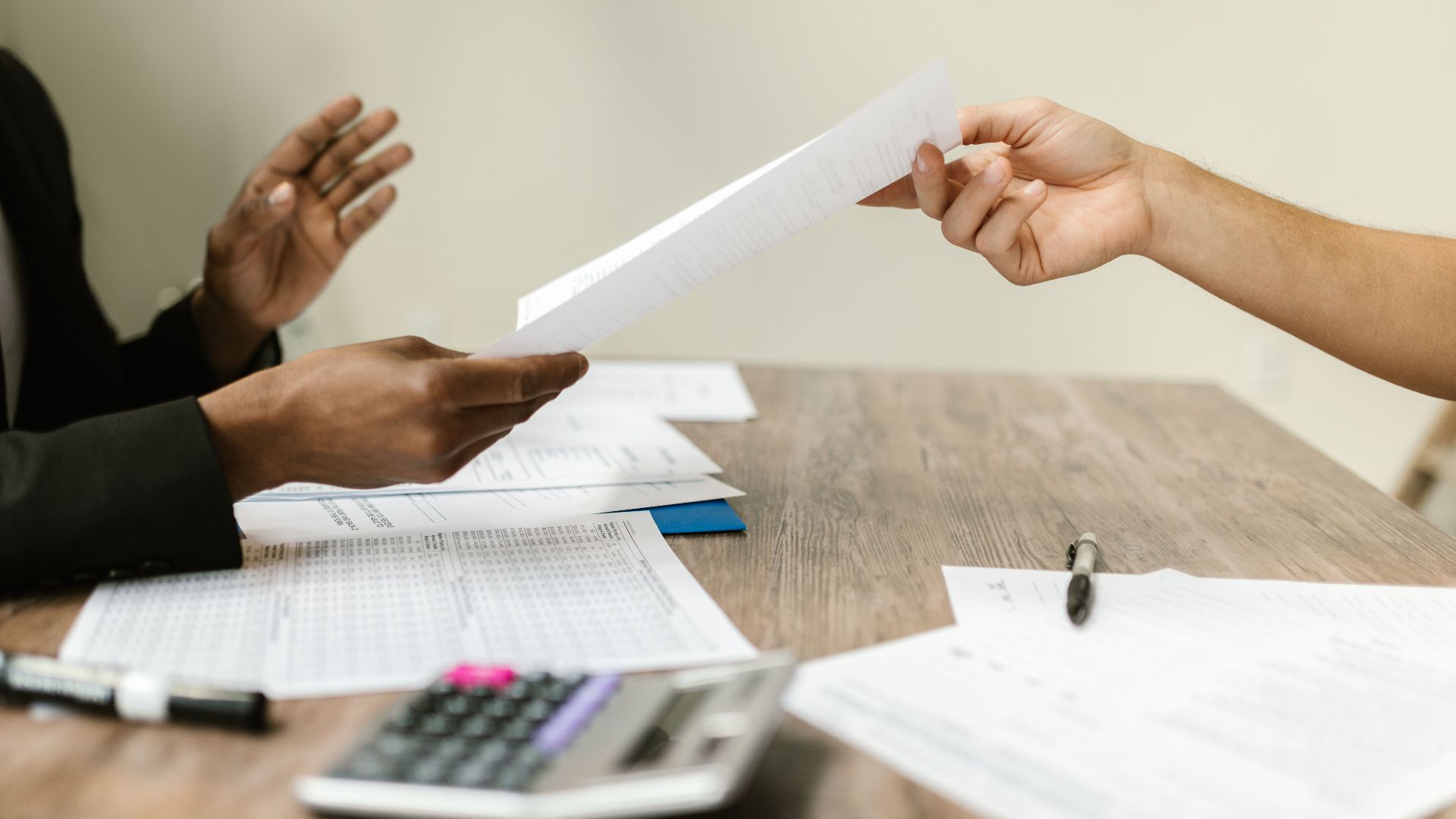 Two professionals exchanging documents in a corporate setting, emphasizing collaboration and paperwork.