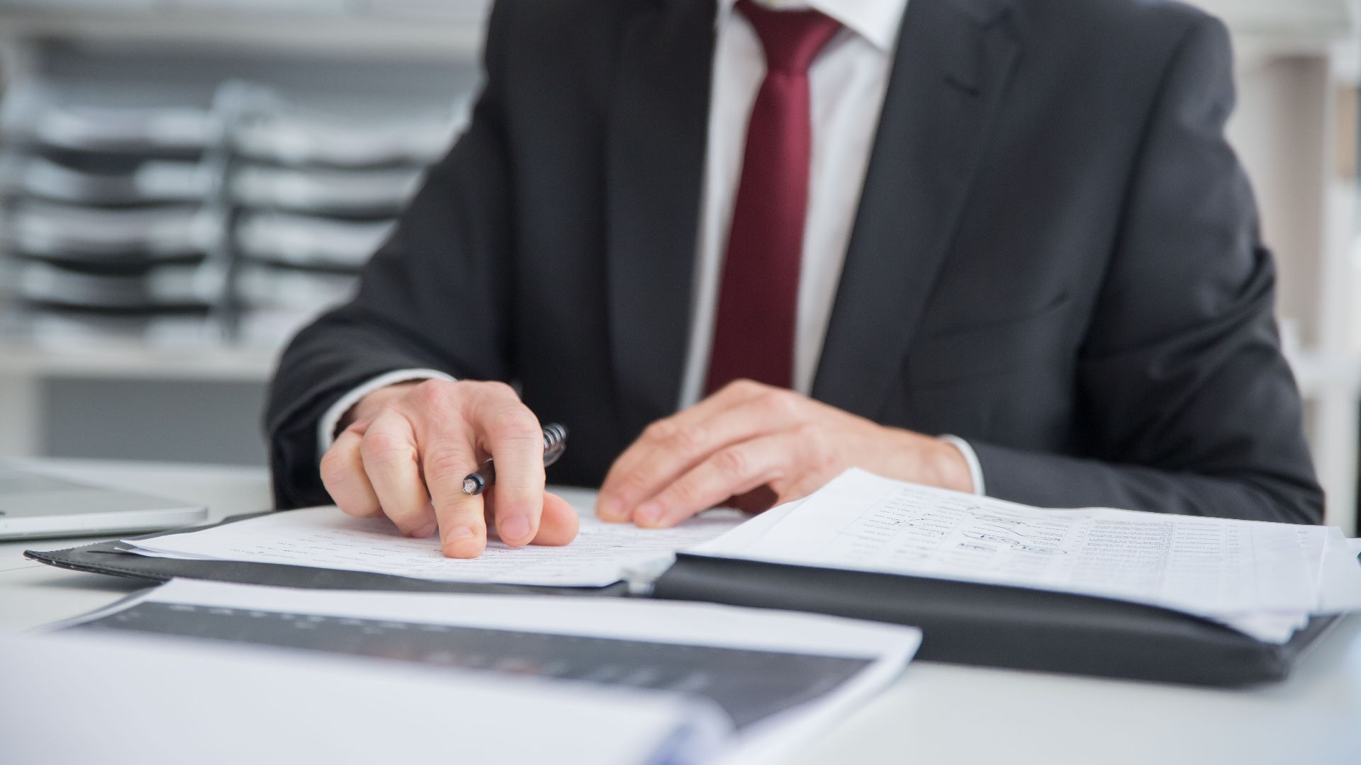 Close-up of a businessman reviewing documents at an office desk. Focus on hands and paperwork.