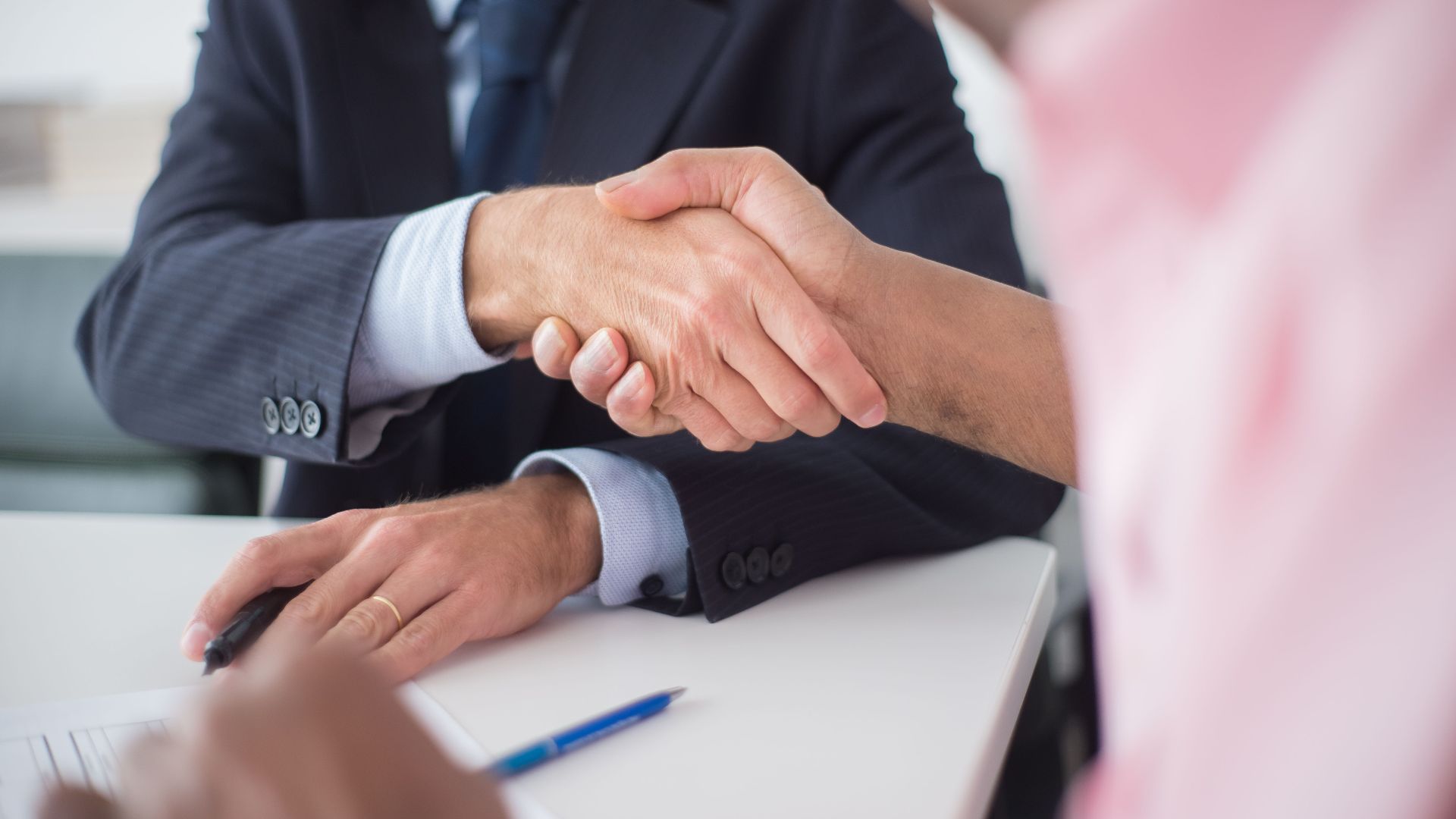 Two businessmen shaking hands across table, symbolizing agreement and partnership in an office environment.