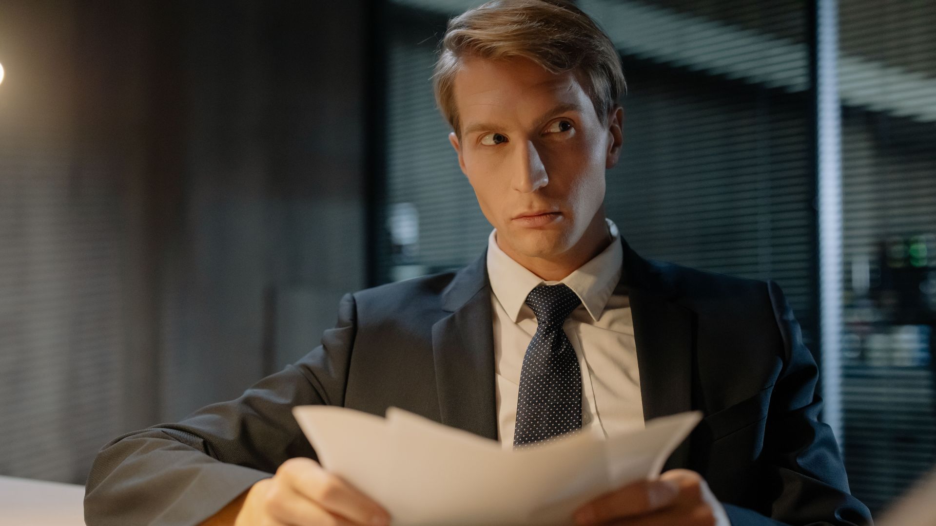 Businessman in suit reviews documents at a desk in a modern office setting.