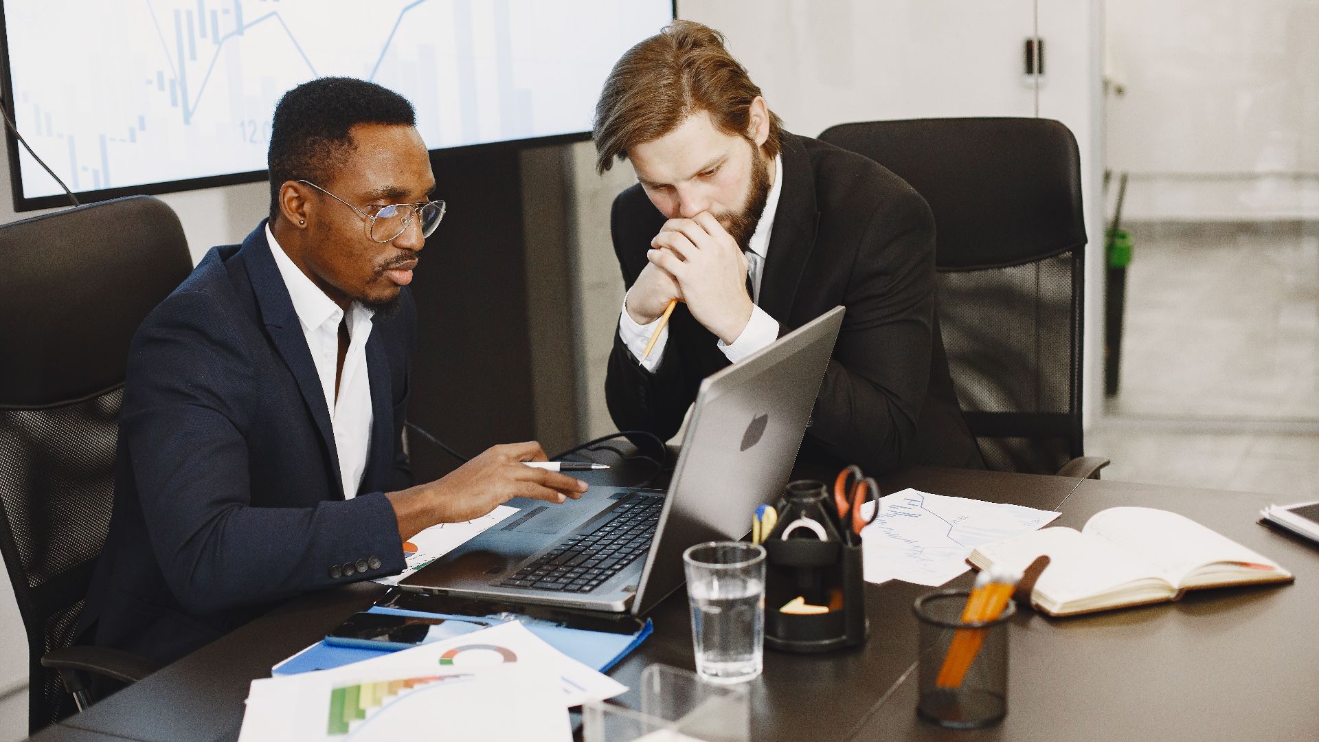 Two businessmen engaged in a strategy meeting with laptops and charts.