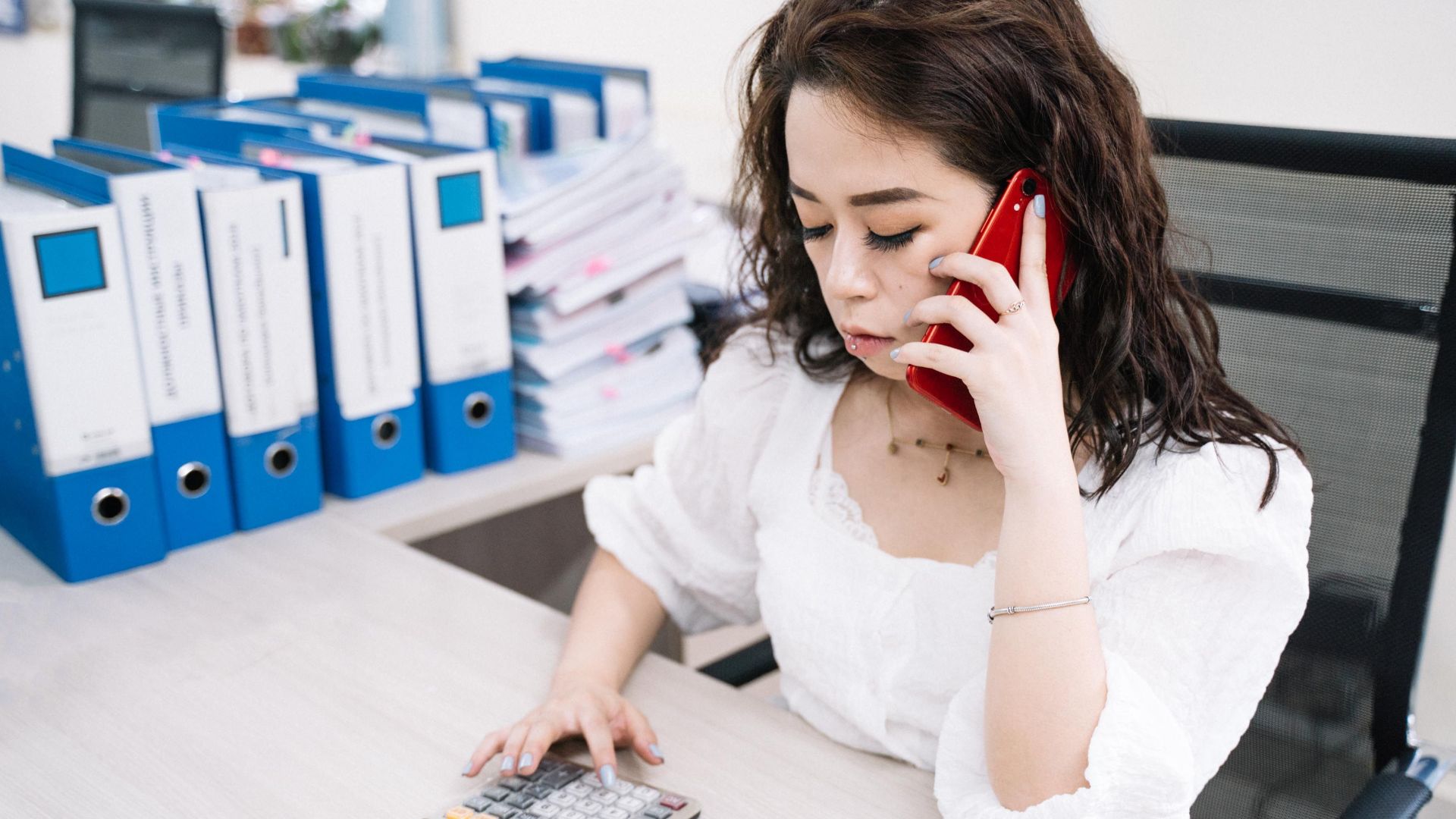 Businesswoman multitasking with calculator and cell phone at office desk.