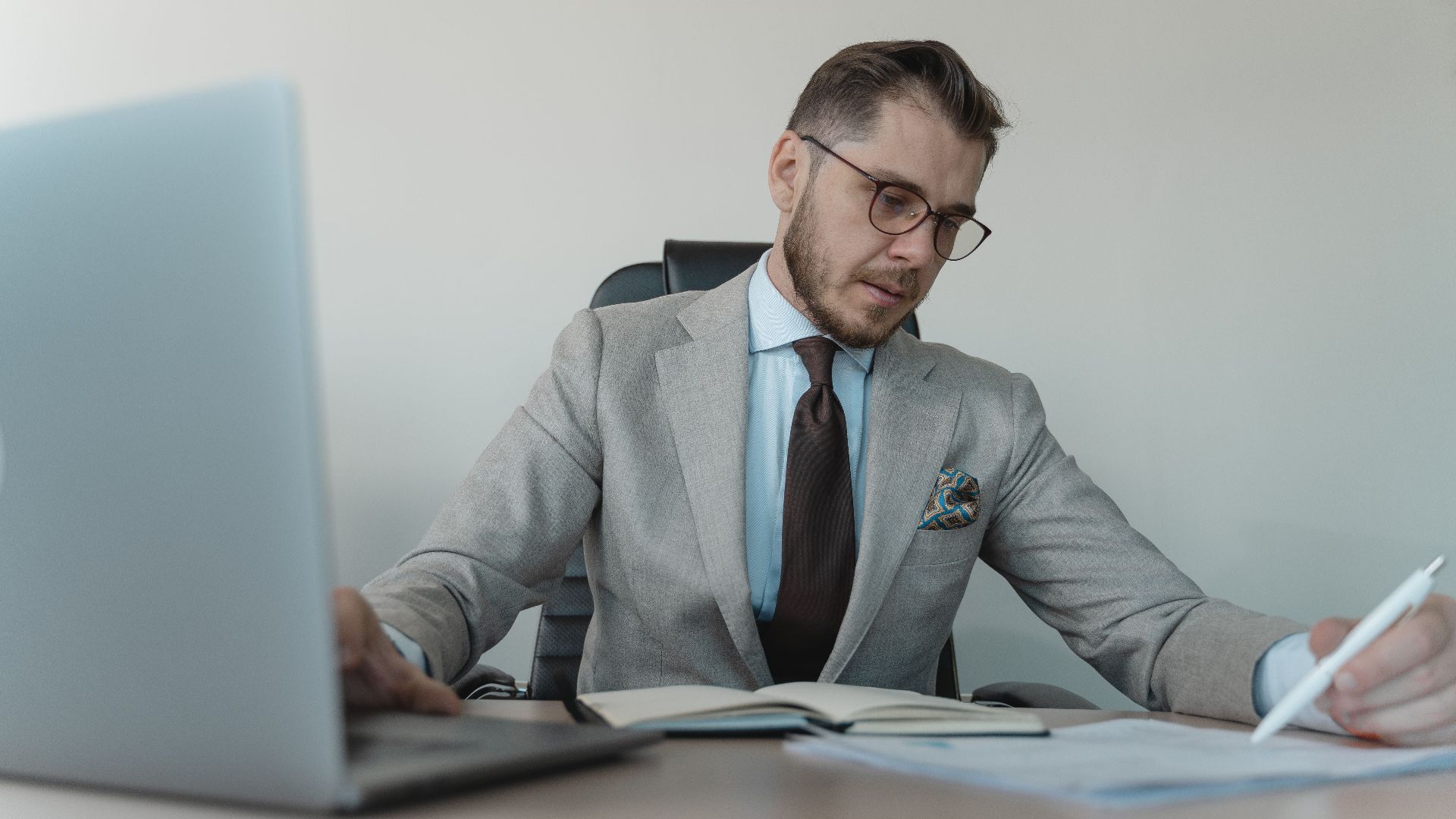 Professional businessman in gray suit working with documents and laptop in modern office.