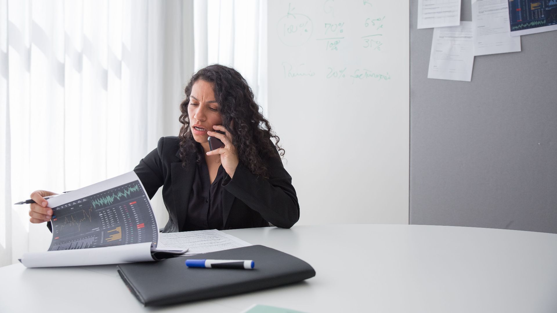 Focused businesswoman reviewing data charts during a phone call in a modern office setting.