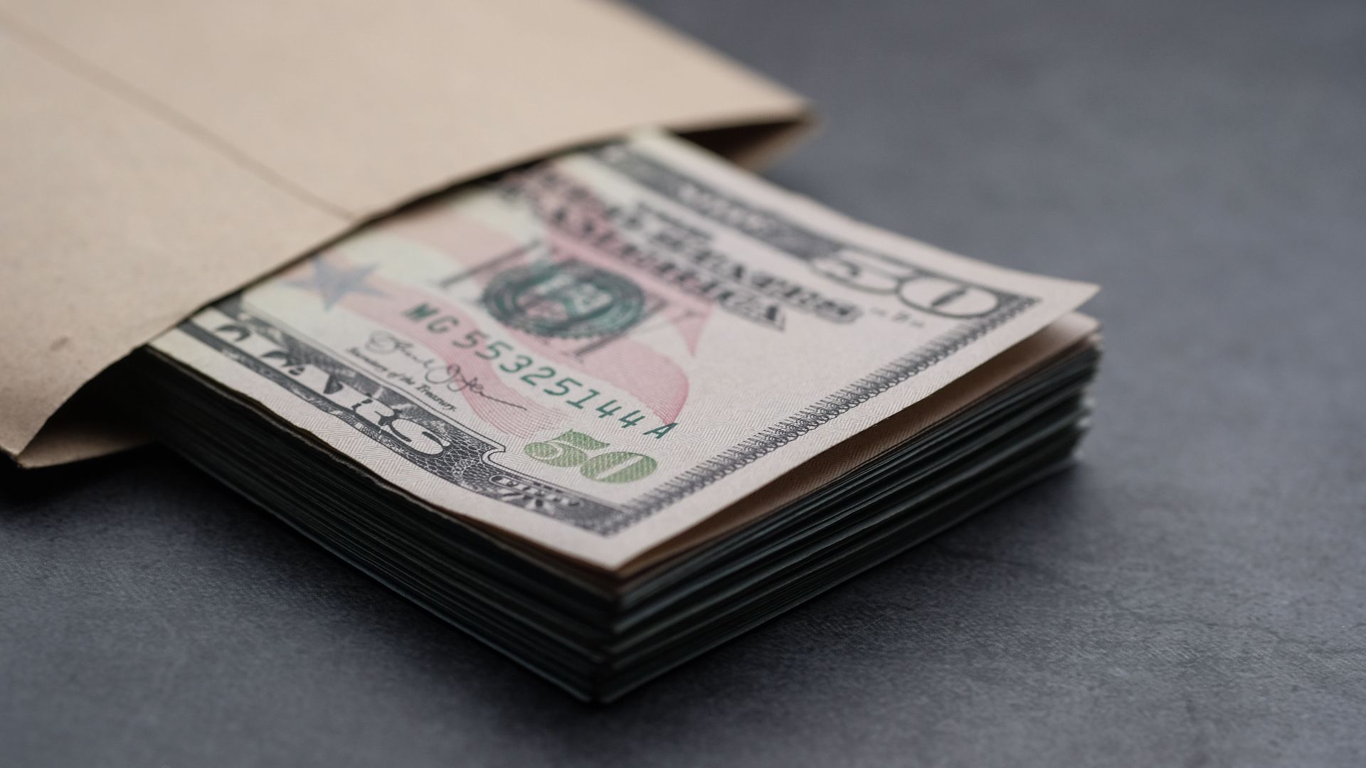 Close-up of US fifty dollar bills partially enclosed in a brown envelope, symbolizing finances.