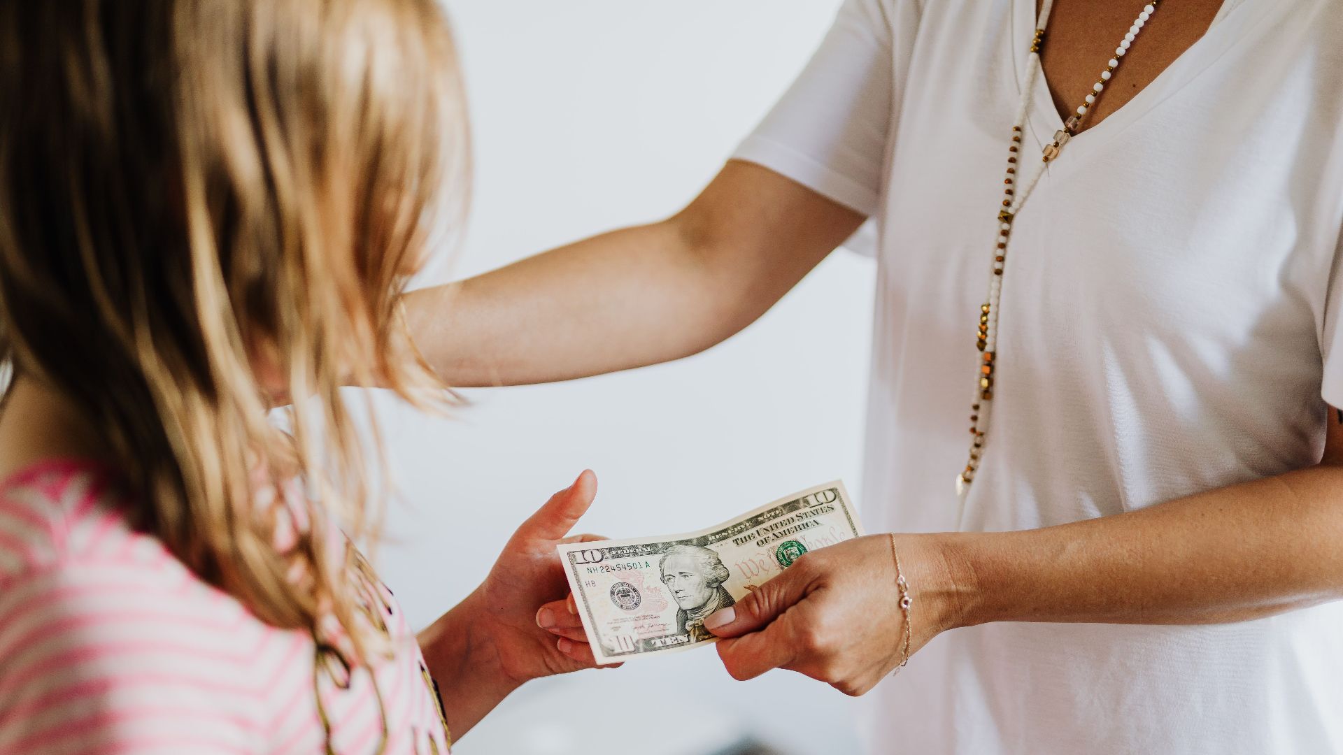 A woman handing money to a young girl, symbolizing family financial education and transactions.